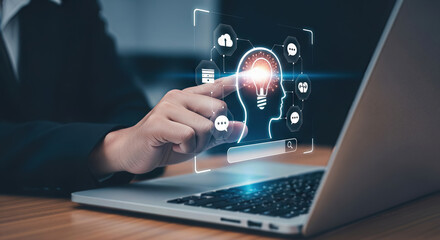 A person touches a laptop screen displaying a holographic outline of a head with a glowing lightbulb inside, representing an idea or innovation