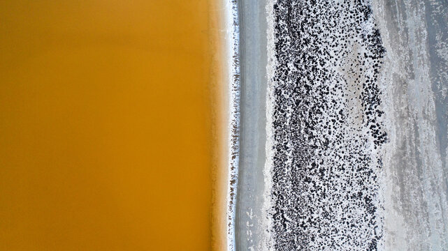 Aerial view of golden waters meeting textured earth in a stark contrast of color and form, Wheatbelt, Western Australia, Australia.