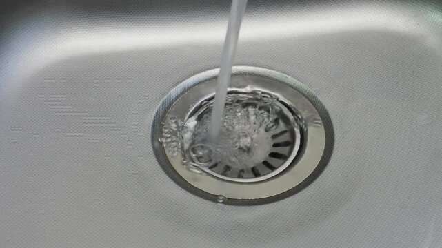 Clean water pours uselessly into a metal sink in the kitchen close-up waste of water