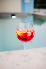 Red cocktail with orange slices and ice cubes by the pool