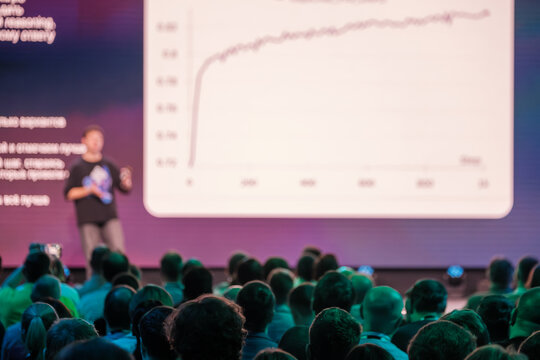 Conference session showing presenter explaining data on screen while audience pays attention