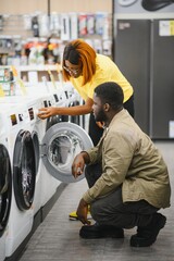 Fototapeta premium Happy smiling young african american couple choosing washing machine in hypermarket