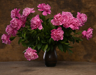 Bright pink peonies in a rustic vase against a textured brown background during soft afternoon light