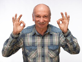 Elderly man smiling and making hand gestures of approval indoors in a bright environment