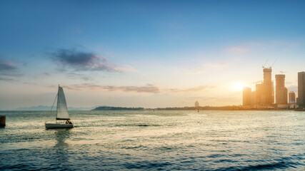 Sailboat on calm sea with city skyline at sunset