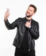 Man smiling while taking a selfie in a casual indoor setting with a black leather jacket