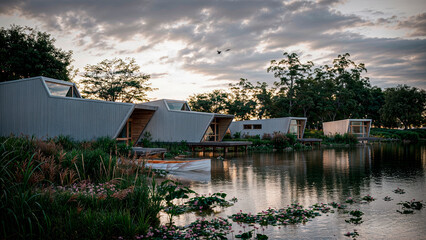 A small modular cabins located near the lake with minimalist architecture and large windows. Set against a clear blue sky and calm coastal environment.