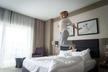 Woman having fun and jumping with bathrobe on bed in hotel room
