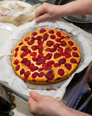 Homemade strawberry cheesecake being lifted from the baking tray in a kitchen