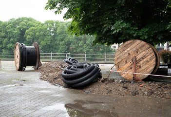 Coiled cables and wooden spools near a green park area with trees during a cloudy day