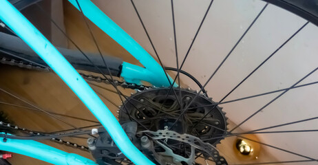 Close-up of a bicycle wheel with a turquoise frame and black spokes. The gear mechanism is visible,...