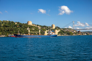 Fototapeta premium Cargo Ship Passing by Rumeli Fortress and Bosphorus Bridge in Istanbul
