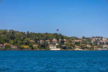 Fototapeta premium Turkish Flag Above the Bosphorus Hills in a Lush Coastal Neighborhood