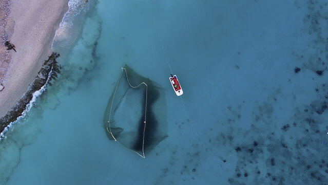 Aerial view of a boat floating on turquoise waters next to a dark net, contrasting with the sandy beach, Kralendijk, Bonaire, Caribbean Netherlands.