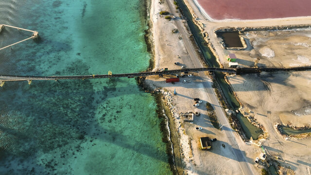 Aerial view of a bridge slicing through turquoise waters next to pink salt ponds, creating a striking contrast of colors and textures, Kralendijk, Bonaire, Caribbean Netherlands.