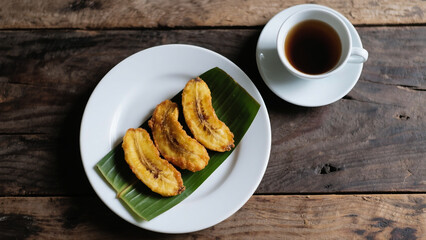 Flatlay of pisang goreng  (fried Banana) with hot drink on wooden table, warm and inviting local snack moment.