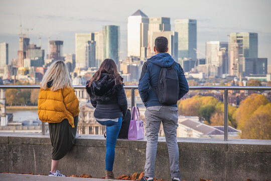 Back view of unidentified tourists appreciating the cityscape of Canary Wharf in London, from Greenwich hill viewing platform 