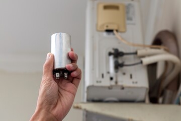 Replacing the Air Conditioner capacitor. Hand holding an AC capacitor.