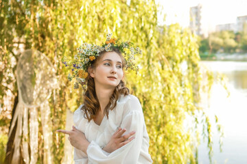 Girl in a wreath against the background of a river at sunset.