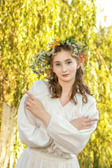 Girl in a wreath against the background of a river at sunset.