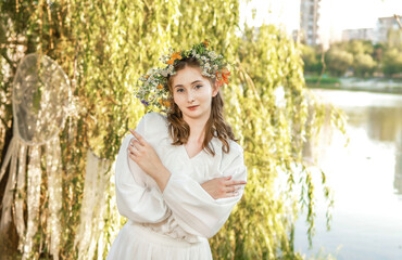 Girl in a wreath against the background of a river at sunset.