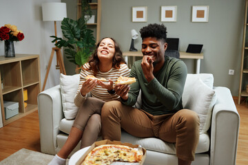 Happy couple laughing and eating pizza on sofa at home