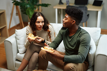 Happy couple enjoying pizza on sofa at home