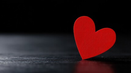 Minimal red heart resting on dark glossy background, evoking love and emotional simplicity