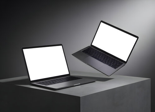 Two silver laptops with blank white screens on a gray concrete surface against a gradient background