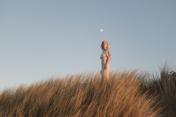 A peaceful scene depicts a woman standing in golden grasses beneath a clear evening sky, radiating...