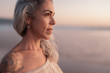 A tranquil moment captured as a woman with a tattoo gazes peacefully at the ocean during sunset,...