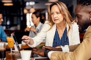 Businesswoman and coworker talking about work while using laptop in modern coffee shop.