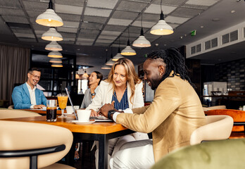 Businesswoman and coworker talking about work while using laptop in modern coffee shop.