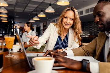 Businesswoman and coworker talking about work while using laptop in modern coffee shop.