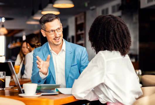 Businessman and female coworker talking about work while using laptop in modern coffee shop.