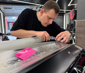 A car wrapping specialist applies a polyurethane film to the car. Detailer smoothes PPF. Car wrapping, detailing, tuning and styling. Selective focus. PPF protective film against chips and scratches. 