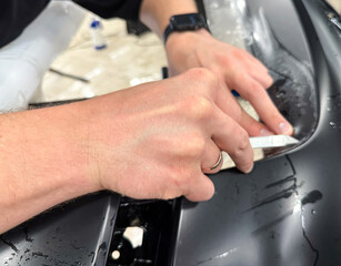 A car wrapping specialist applies a polyurethane film to the car. Detailer smoothes PPF. Car wrapping, detailing, tuning and styling. Selective focus. PPF protective film against chips and scratches. 