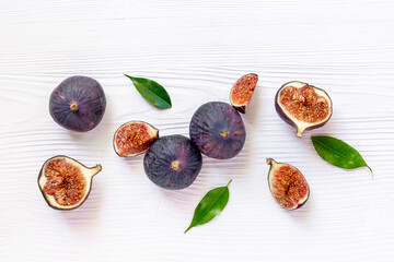 Purple ripe figs fruit and slices with green leaves top view on a wooden background