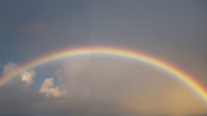 A colorful rainbow arcs across the blue sky with clouds, highlighting the beauty of nature after the rain