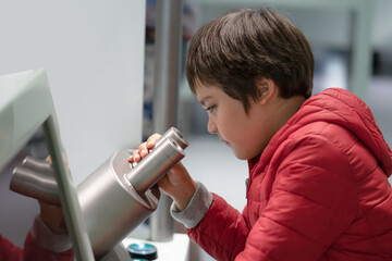 Curious School boy looking through microscope in science exhibition or educational Center.Child...