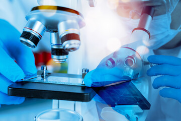 Scientist adjusting microscope and slide in laboratory with blue light for medical research and...