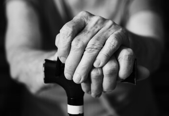 Senior man and young caregiver holding hands on walking stick. Shallow depth of field. Toned image, black and white