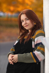 Portrait of a young beautiful cheerful red-haired girl in an evening autumn city.