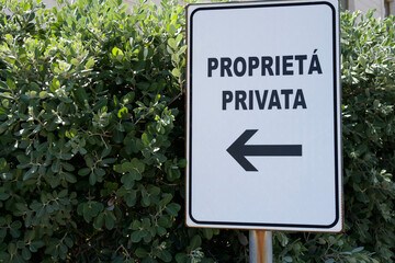 Private property sign indicating direction with lush green foliage in the background and clear blue sky above