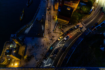 Overhead shot of a riverside street at night, showing cars, people, and illuminated buildings.
