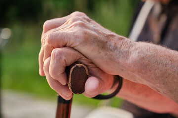 Senior man and young caregiver holding hands on walking stick. Shallow depth of field.