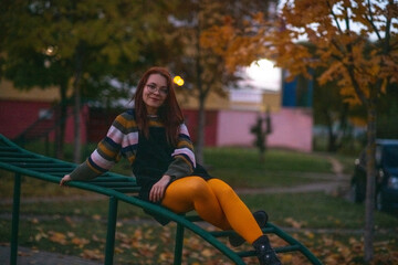 Portrait of a young beautiful cheerful red-haired girl in an evening autumn city.