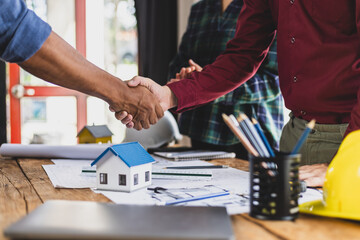 Architect holding blueprints is shaking hands with a client in his office during a meeting about a real estate project.