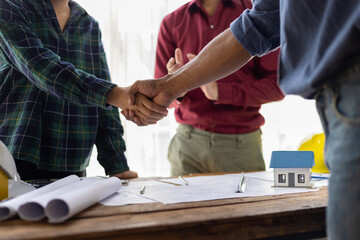 Architect holding blueprints is shaking hands with a client in his office during a meeting about a real estate project.