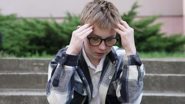 Sad boy sitting outside in a bad mood after school. Childhood depression, headaches and migraines, bullying.